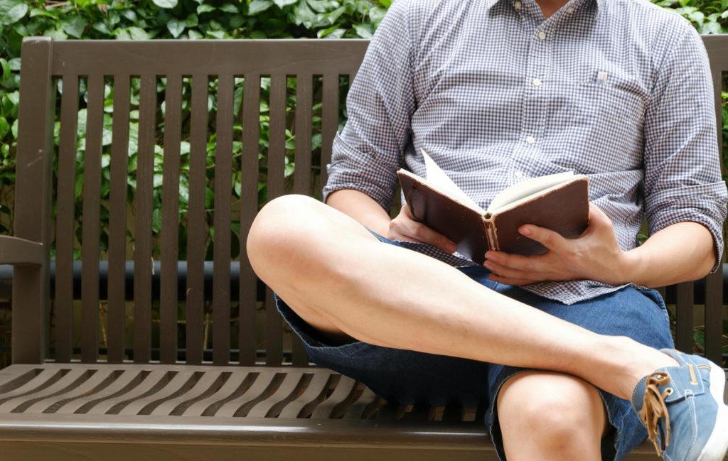 Man in park reading about vulnerability and masculinity, alongside two men embracing with a firm back pat, symbolizing emotional connection and vulnerability in Maryland and DC.