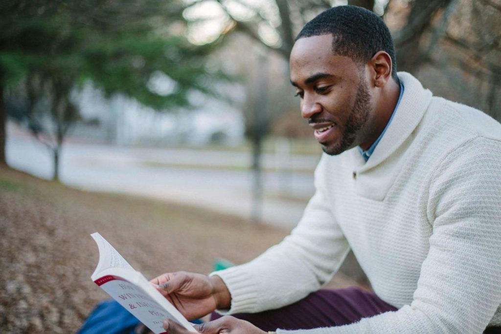 A man after a March Madness game, reading about a child climbing a tall tree with sunlight filtering through, symbolizing emotional growth and men who Shut Down Emotion in Maryland and DC.