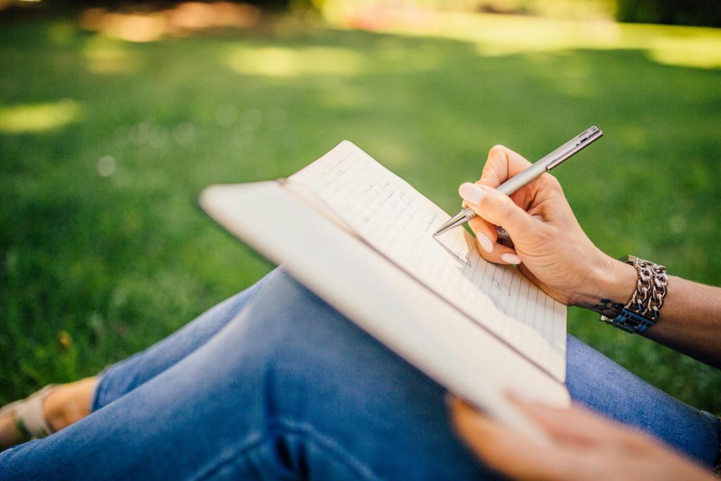 Woman writing outside in in summer in an old notebook, symbolizing nostalgia and emotional connection in Maryland and DC.