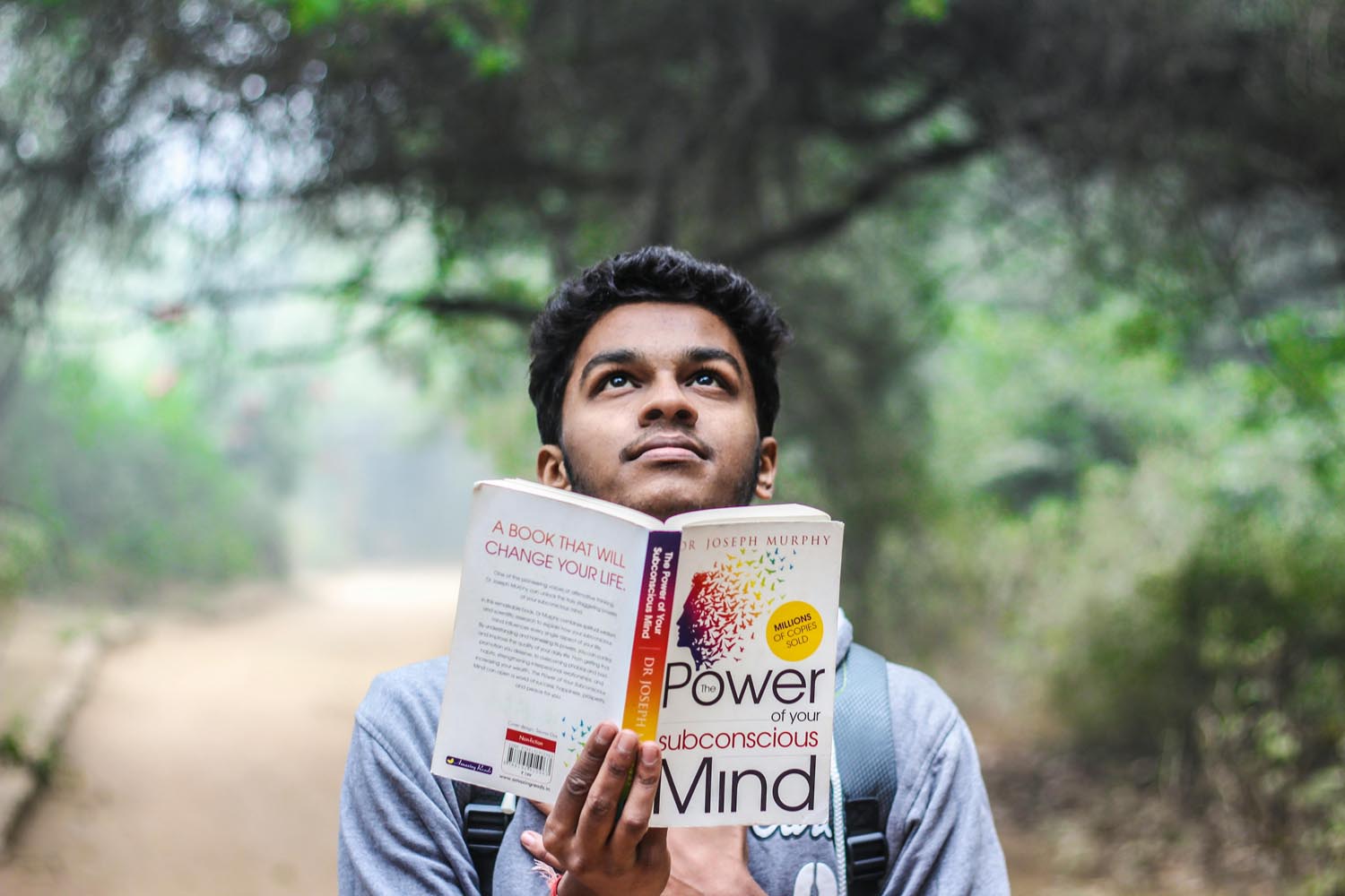 Student sitting on a college campus with a book about fatherhood, symbolizing Understanding Men’s Emotional Lives and independence in Maryland and DC.